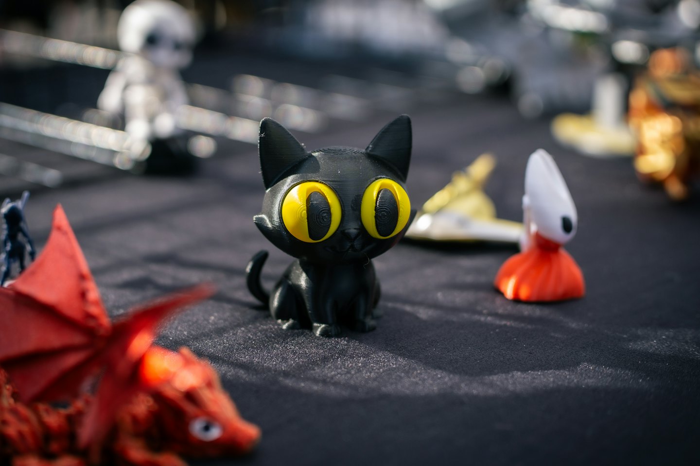 Schwarze 3D-gedruckte Katze mit gelben Augen sitzt auf einer grauen Oberfläche.
